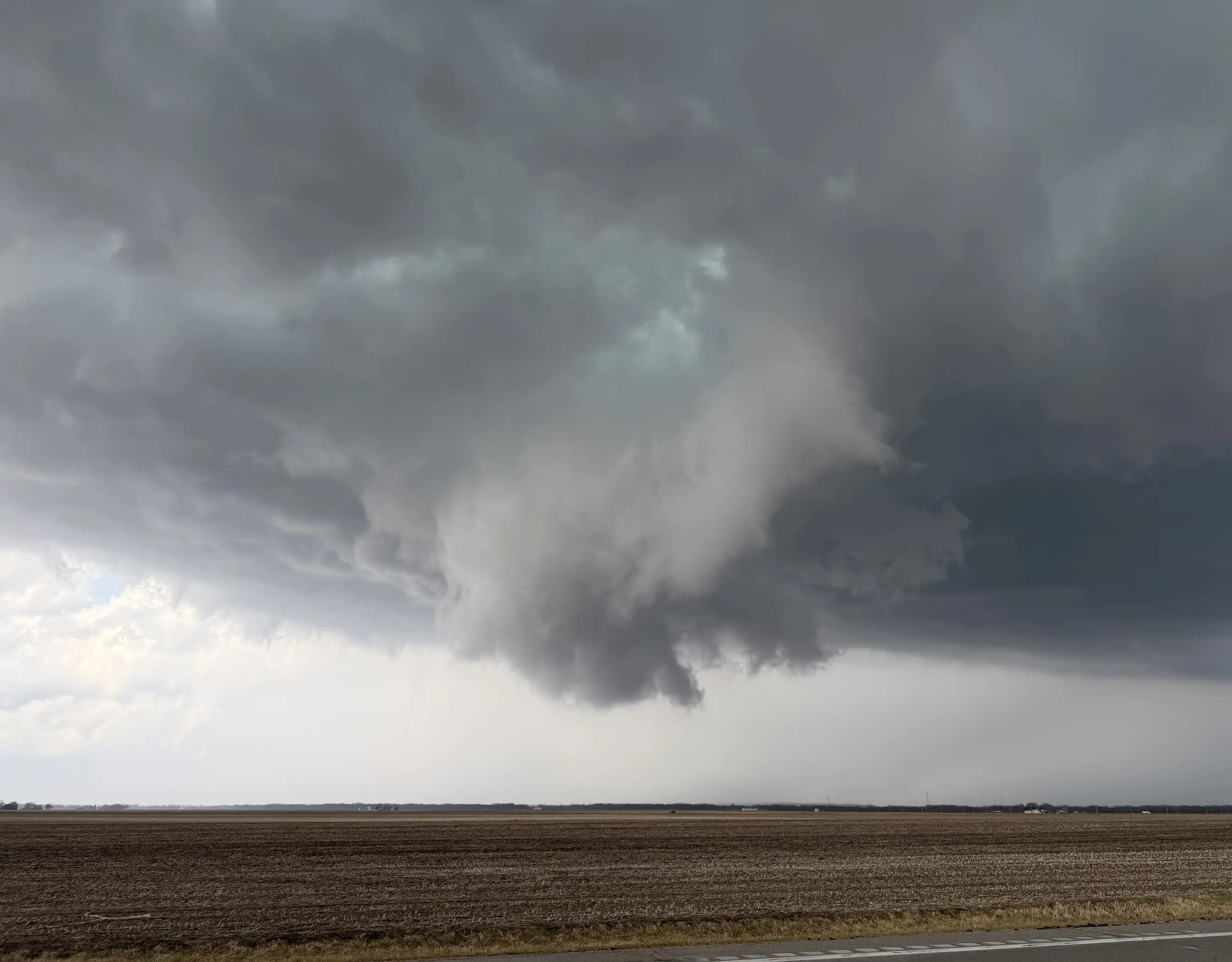 A wall cloud hanging beneath a dark storm base over open farmland near Pontiac, Illinois.